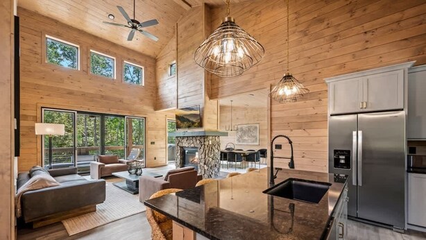 A modern kitchen with a large island, stainless steel appliances, and a dining area with a stone fireplace. - Starlight Ridge - Indoor pool & theater room (Smoky Mountains)