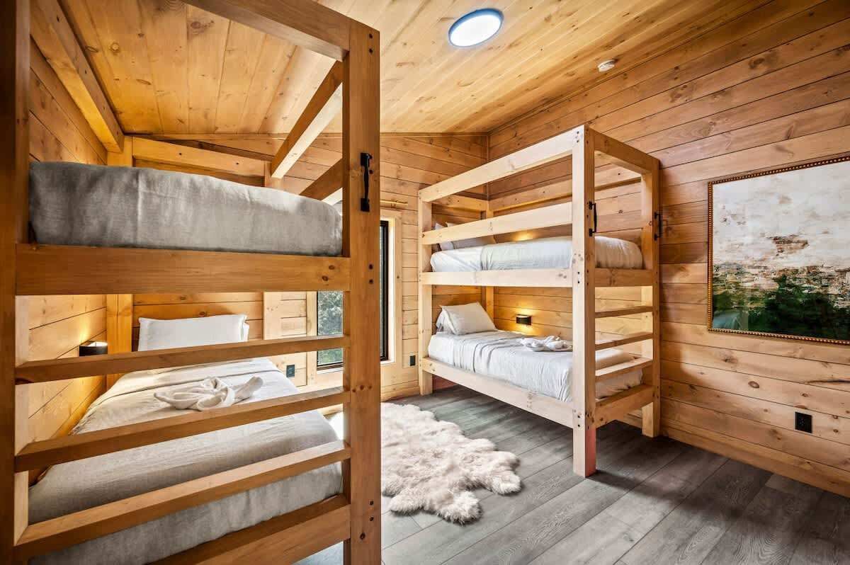 L’intérieur d’un chalet en bois, avec des lits superposés, un tapis en fourrure et un tableau accroché au mur.