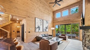 A spacious wooden interior with a staircase, a sofa set, a dining table, and a stone fireplace. - Starlight Ridge - Indoor pool & theater room (Smoky Mountains)