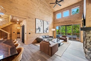 A spacious wooden interior with a staircase, a sofa set, a dining table, and a stone fireplace.
