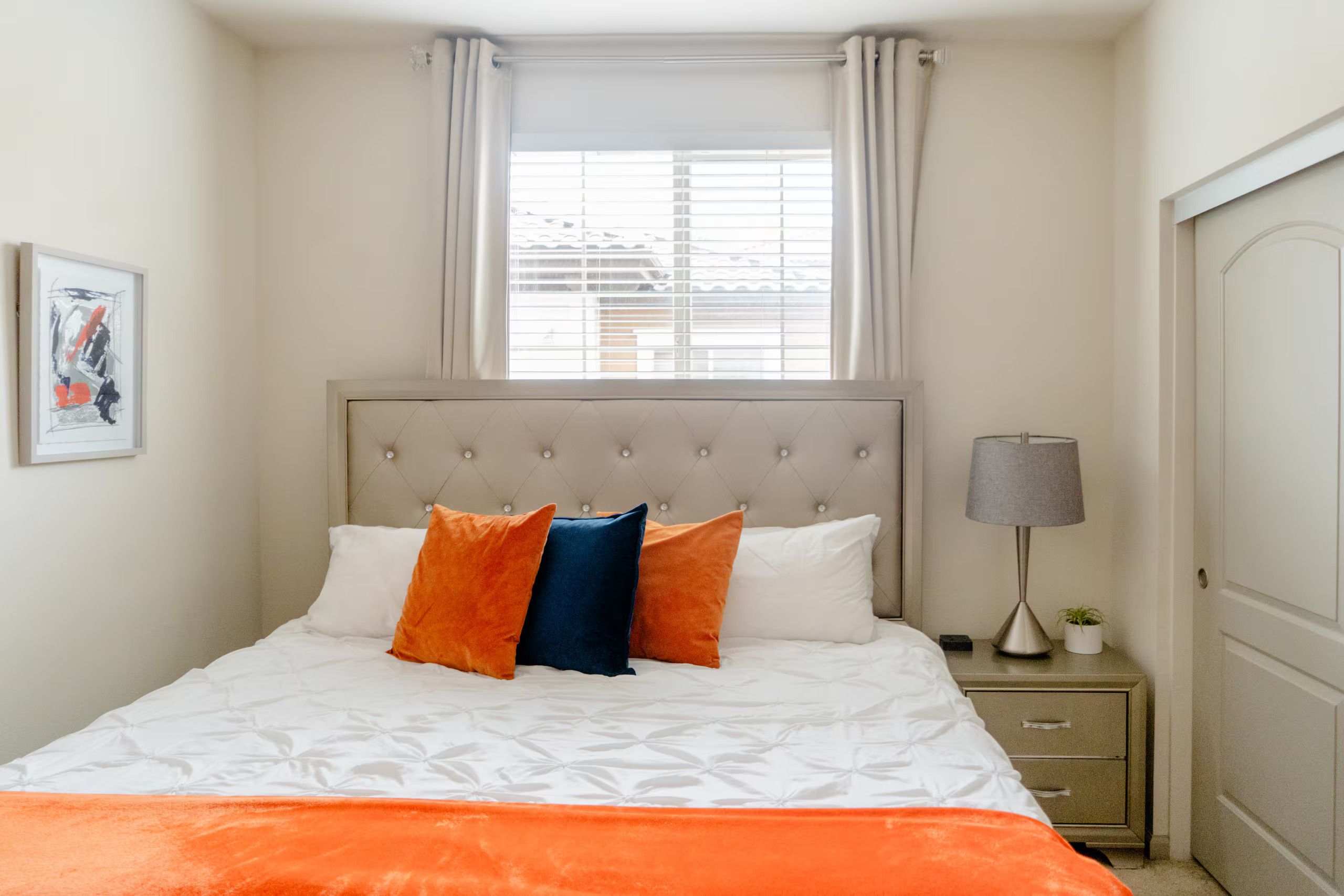 Un dormitorio con una cama, una mesita de noche, una lámpara y una ventana con cortinas.