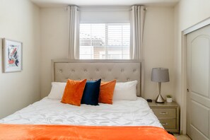 A bedroom with a bed, a nightstand, a lamp, and a window with curtains.