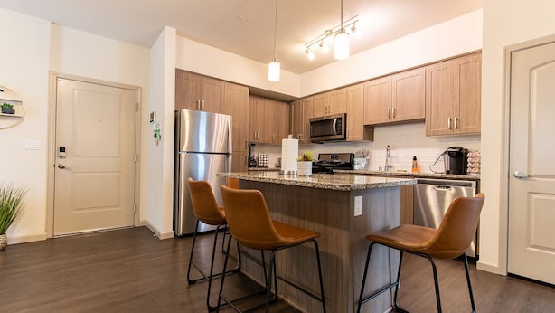 A modern kitchen with wooden cabinets, stainless steel appliances, and a central island with bar stools.