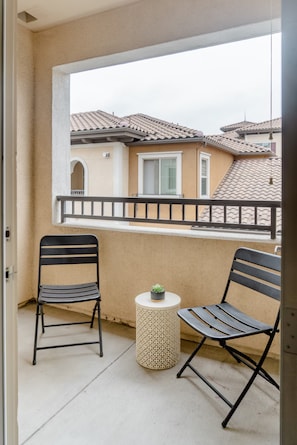 A balcony with two chairs and a small table, overlooking a residential area with tiled roofs.