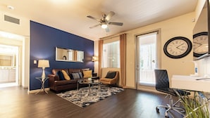 A modern living room with a dark wood floor, a ceiling fan, a sofa set, a coffee table, and a desk with a chair.