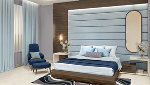 A modern bedroom with a large bed, a ceiling fan, a side table with a lamp, and a chair. - Cygnett Inn  (Kishangarh)