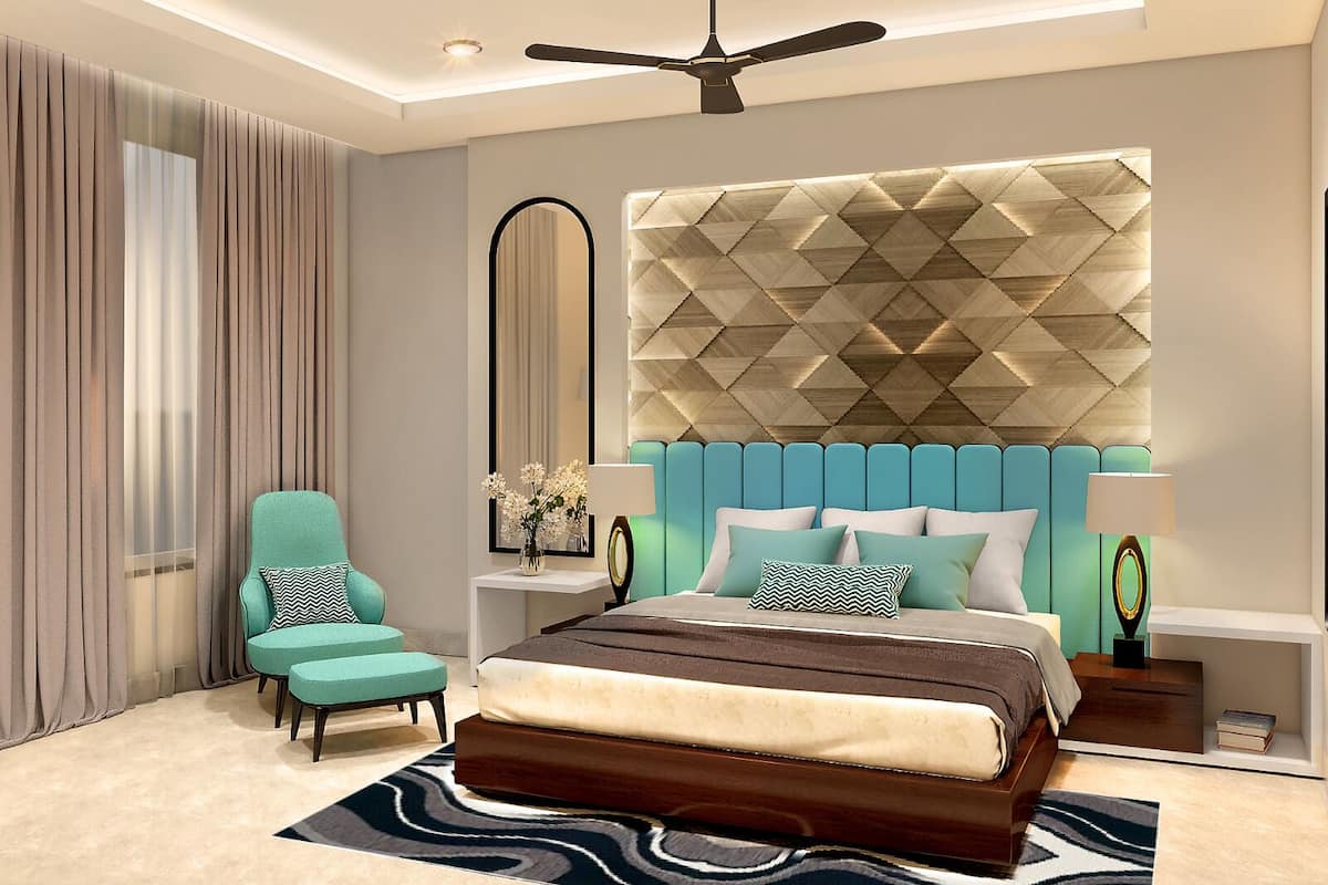 Un dormitorio moderno con un cabecero capitonado, un sillón azul verdoso, una cama grande con muchas almohadas, una mesita de noche con lámpara y un ventilador de techo.