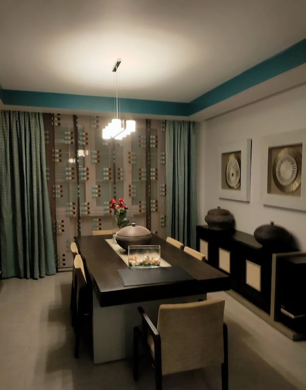 A dining area with a large table, chairs, a vase with flowers, and decorative wall art.