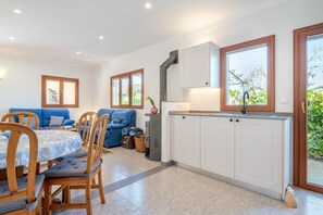 Una cocina moderna con armarios blancos, una estufa y un ventanal. Hay una zona de comedor con una mesa y sillas, y un sofá azul.