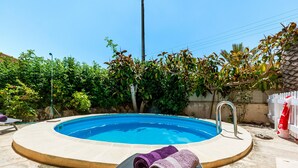 Una piscina con un jacuzzi, rodeada de follaje y una cerca blanca.