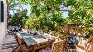 Un área de comedor al aire libre con mesa y sillas de madera, una parrilla y vistas a vegetación exuberante.