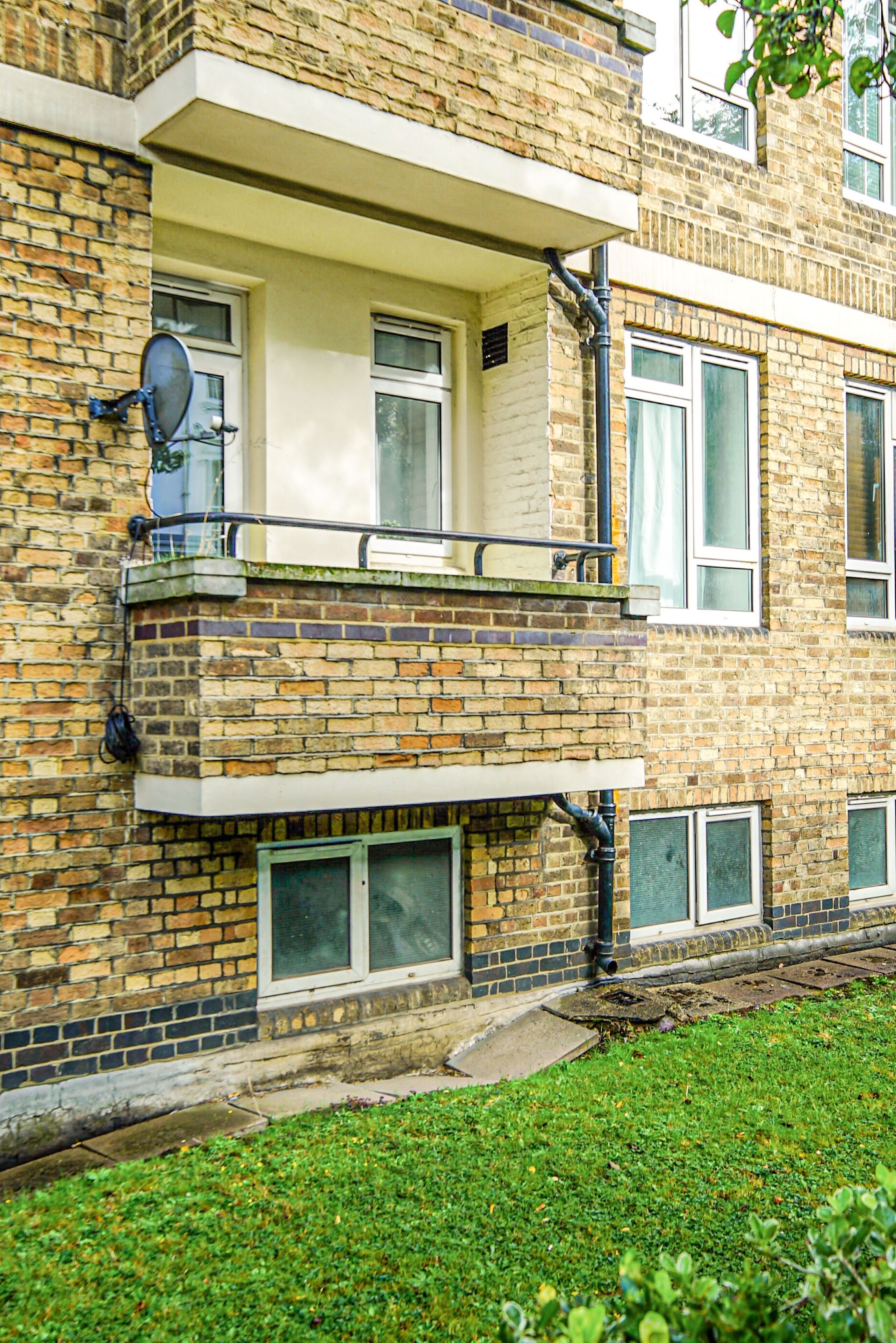Un immeuble de deux étages avec une façade en briques, un balcon doté d’une rambarde en métal et une antenne parabolique sur le côté.