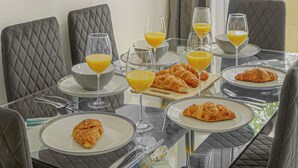 A breakfast table set with croissants, orange juice, and glasses, with a view of the street outside. - Paddington Station 2BR City Apartment (London)