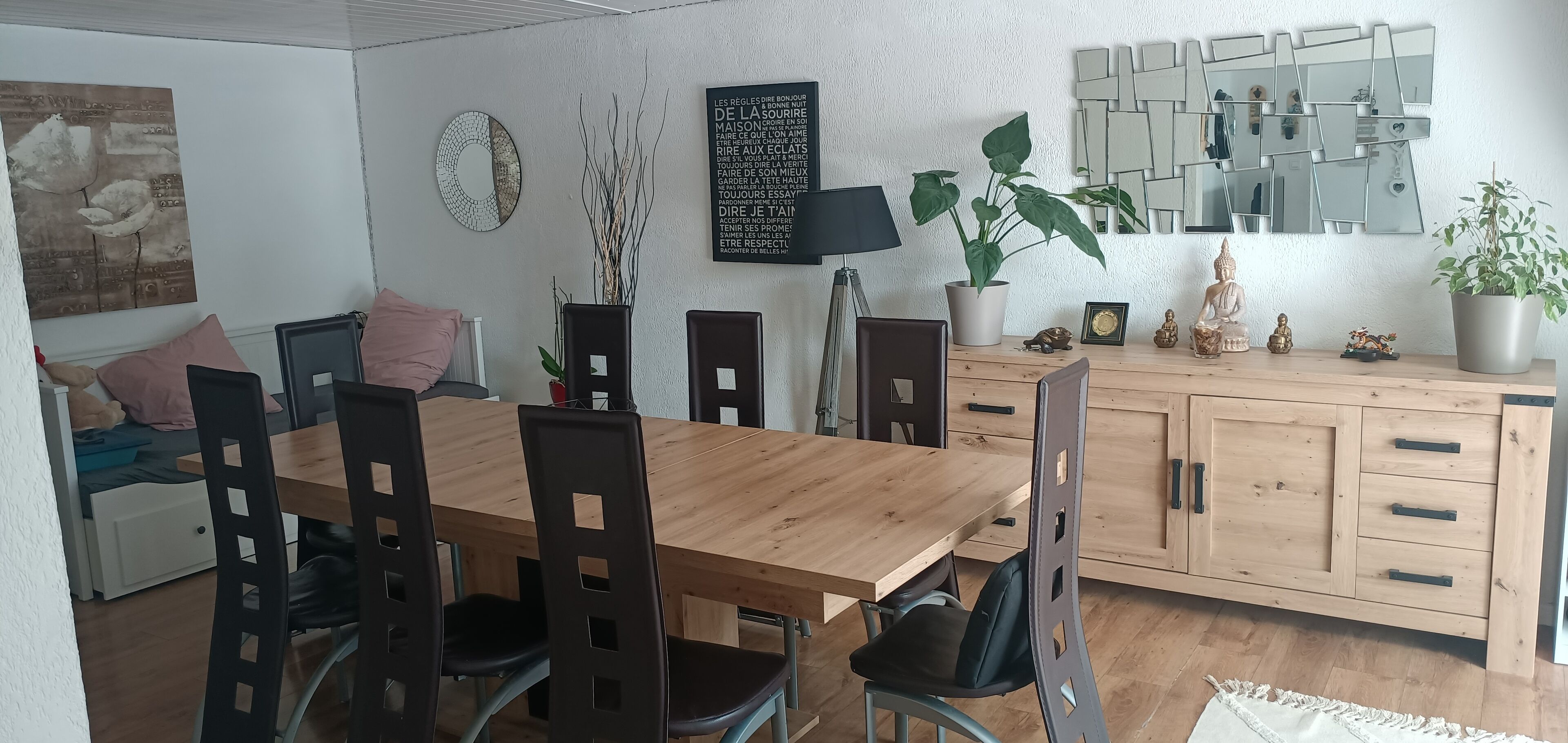 A dining area with a wooden table, black chairs, a potted plant, and a cabinet with drawers.