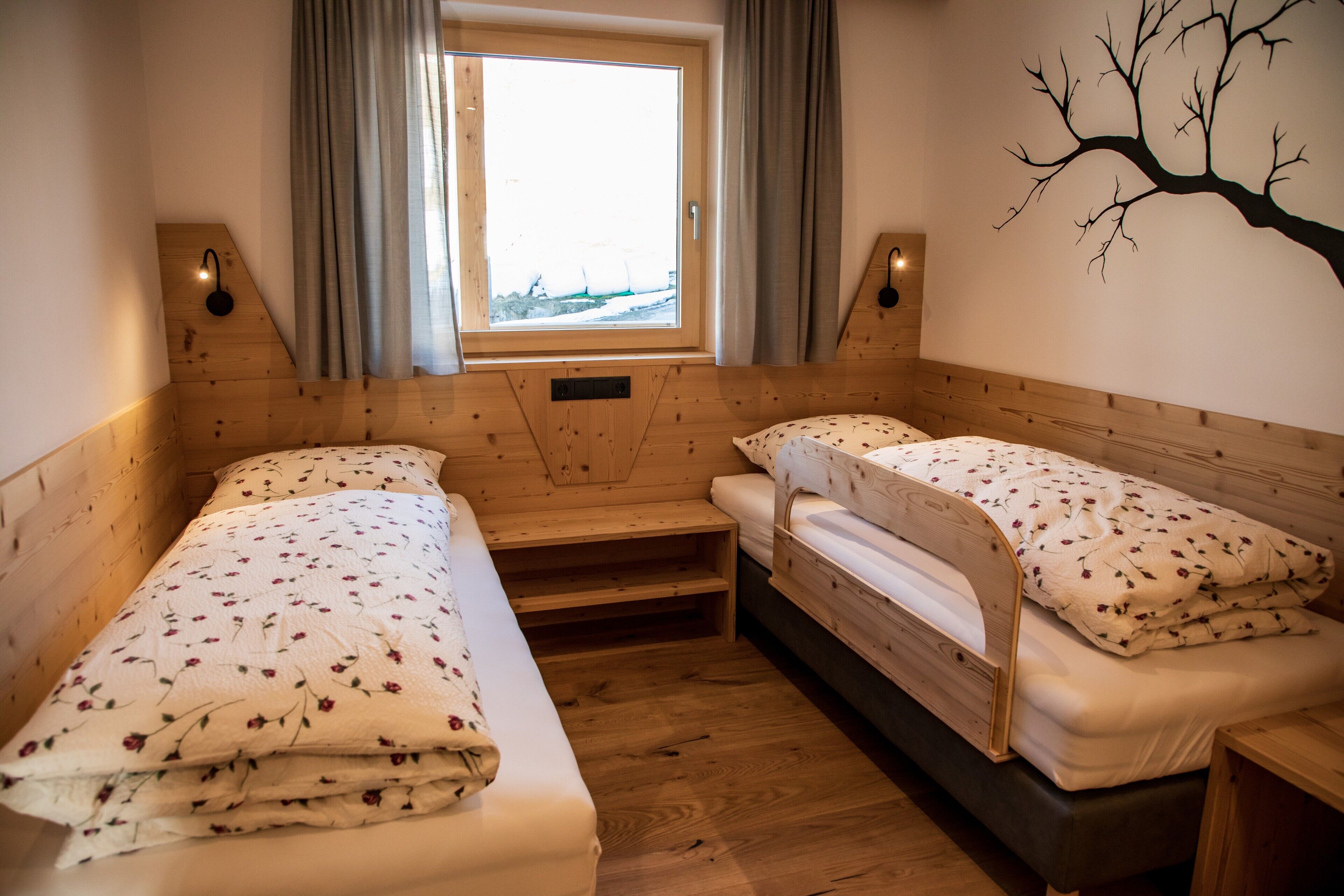 Una habitación acogedora con dos literas de madera, una ventana con cortinas, un adorno de árbol montado en la pared y un pequeño banco de madera.