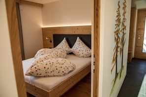A wooden bed with floral pillows, a headboard, and a wall-mounted light fixture.