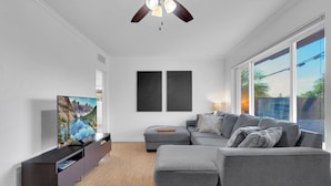 Ein modernes Wohnzimmer mit Flachbildfernseher, grauem Sofa und Deckenventilator.