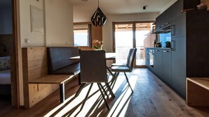 A modern kitchen with wooden flooring, a dining area with a bench, and a view through the window.