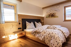 Un dormitorio con cabecera de madera, cama con ropa de cama floral, un pequeño banco y una pintura de montañas en la pared.