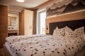 Une chambre avec une tête de lit en bois, un lit recouvert d’une literie à motifs floraux, une armoire en bois et une fresque représentant une montagne sur le mur.