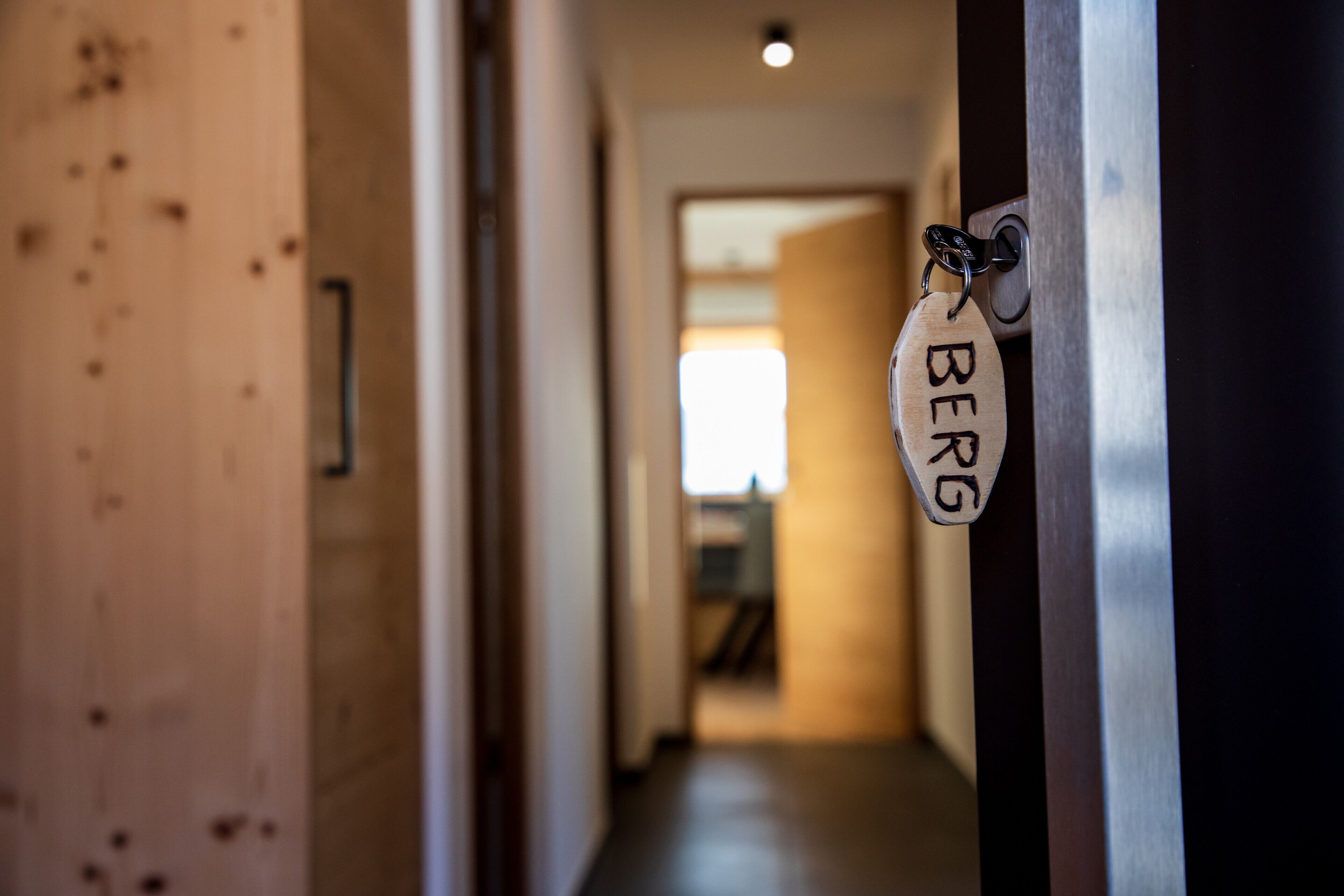 A hallway with a wooden door, a keychain with 'BERG' on it, and a bright window in the distance.
