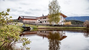 A lakeside hotel with a wooden exterior, a dining area, and a view of the lake and mountains. - Apartment "Kieserhof Berg" with Mountain View, Private Terrace & Wi-Fi (Terenten)