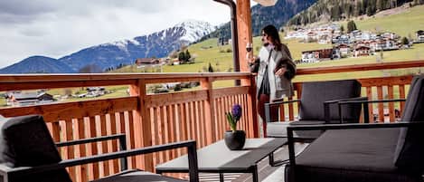 Una terraza de madera con mobiliario exterior, una planta en maceta y vistas a un paisaje montañoso.