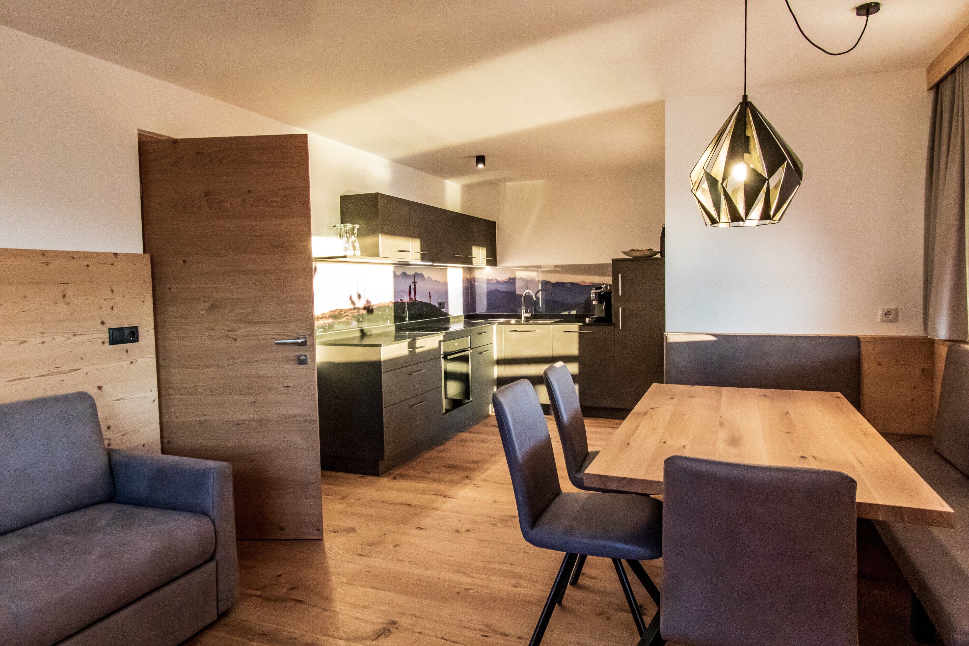 A modern kitchen with a wooden island, a dining area with a wooden table and chairs, and a pendant light.