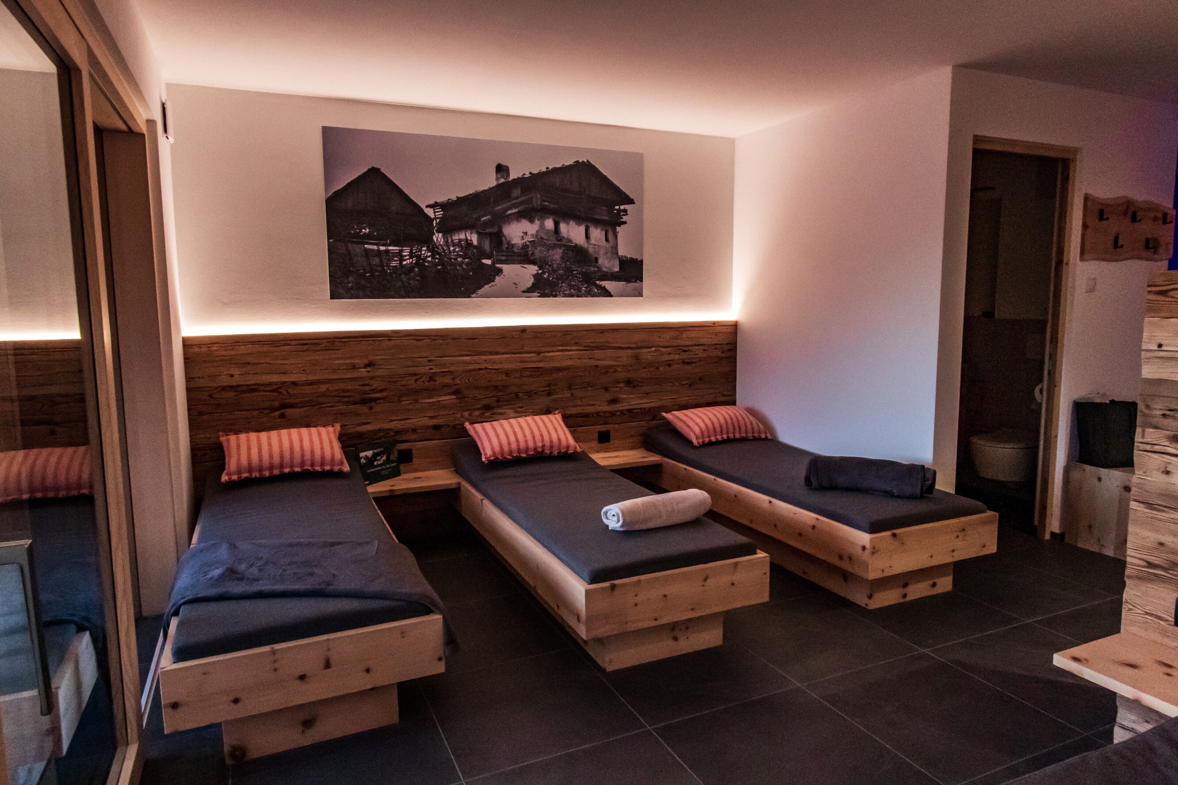Ein Zimmer mit drei Holzbett, einem hölzernen Kopfteil, einem gerahmten Bild an der Wand und einem kleinen Holztisch.