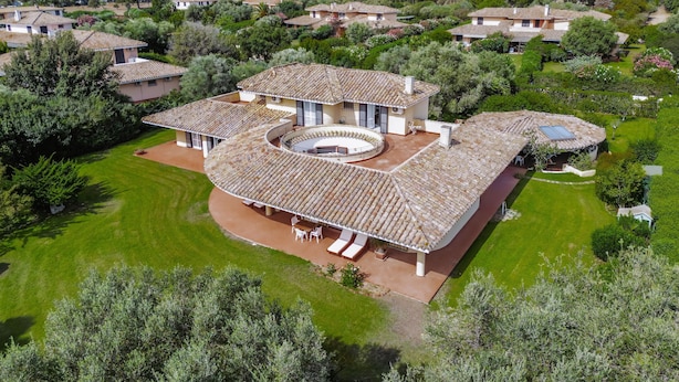 A large, single-story house with a circular patio, surrounded by lush greenery and other houses in a hilly area. - Holiday Home 'Villa Degli Olivi' with Sea View, Garden, Terrace & Wi-Fi (Pula)