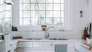 A kitchen with white cabinets, a window with a view of palm trees, a sink, and a checkered towel hanging on the door. - Holiday Home 'Villa Degli Olivi' with Sea View, Garden, Terrace & Wi-Fi (Pula)