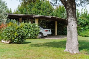 Un abri de voiture fermé, avec une voiture blanche garée à l’intérieur, entouré de verdure et d’arbres.