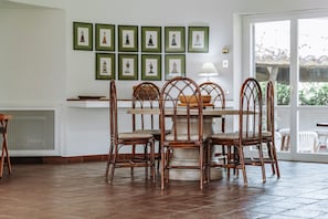 Un coin repas avec une table entourée de chaises en osier, un sol carrelé et des tableaux encadrés accrochés au mur.