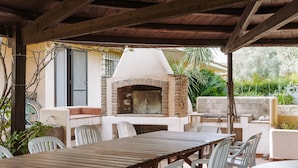 An outdoor patio with a brick oven, white chairs, and a wooden table. - Holiday Home 'Villa Degli Olivi' with Sea View, Garden, Terrace & Wi-Fi (Pula)