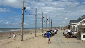 Un restaurant a la vora de la platja amb terrassa, pals de fusta i vista a l'oceà.