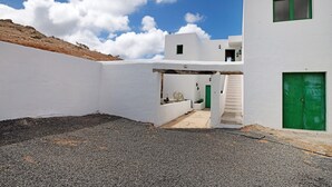 A modern white building with a green door and window, a gravel courtyard, and a clear blue sky.