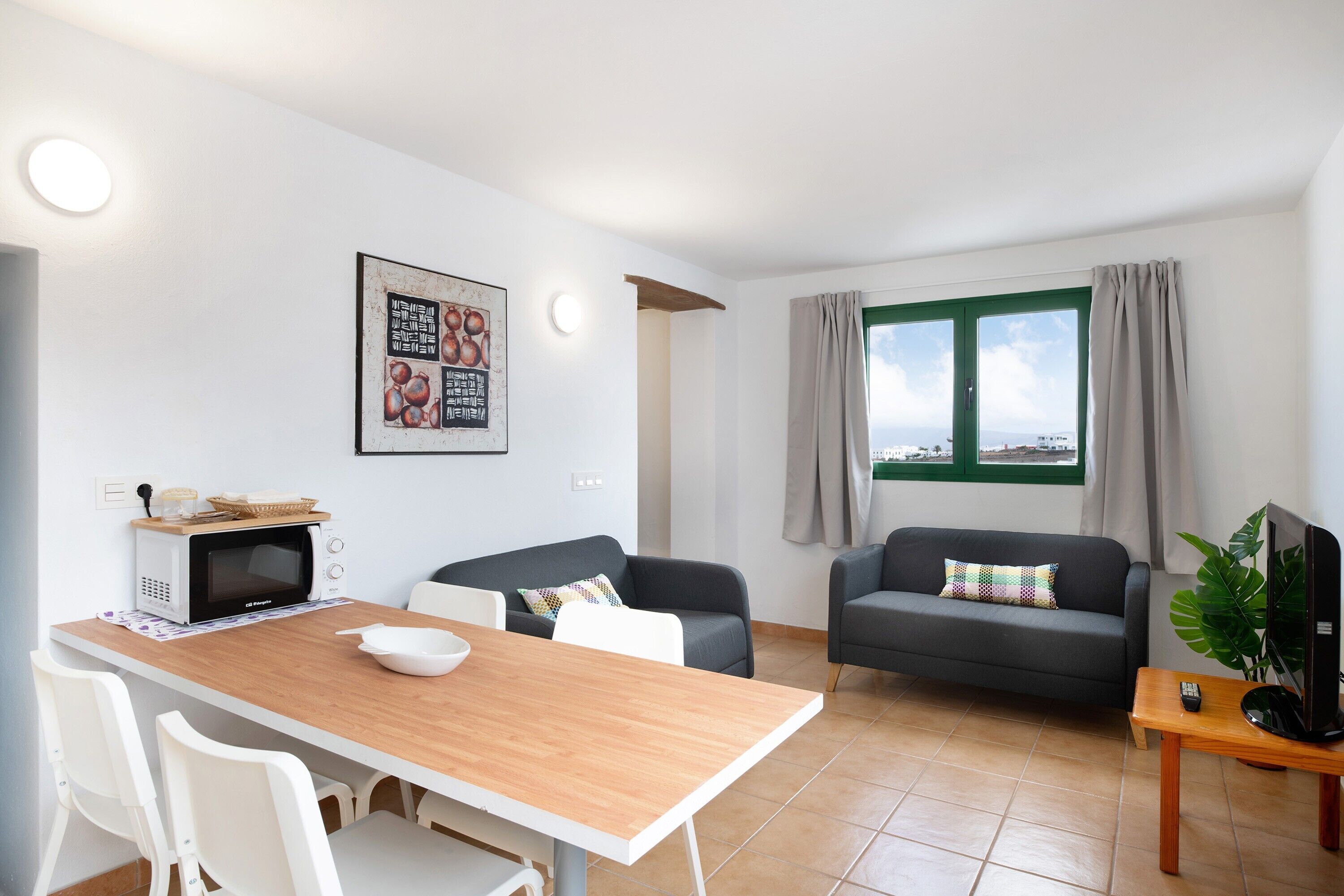 Ein modernes Wohnzimmer mit Essbereich, zwei Sofas, einem Fernseher und einem Fenster mit Vorhängen.