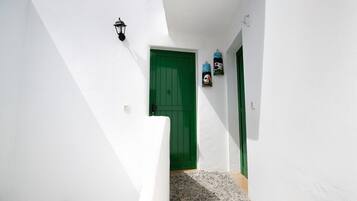 Un edificio de paredes blancas con una puerta verde, un pequeño escalón que lleva a la entrada y una lámpara fijada a la pared.
