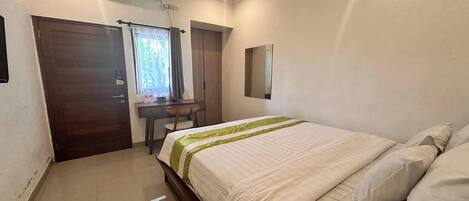 A bedroom with a bed, a desk, and a window with curtains.