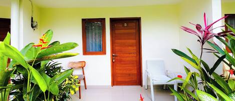 Entrada de casa com porta de madeira, uma cadeira branca e várias plantas.