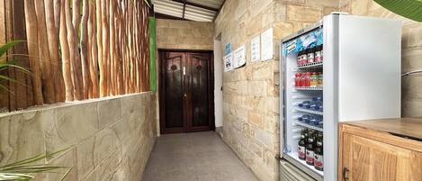 Un pasillo estrecho con pared de piedra, una puerta de madera, un refrigerador lleno de bebidas y un armario de madera.