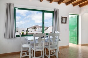 A room with a table and chairs, a window with a view of buildings and mountains, and a green door. - Vacation Home 'San Roque' with Mountain View, Private Terrace and Wi-Fi (TINAJO)