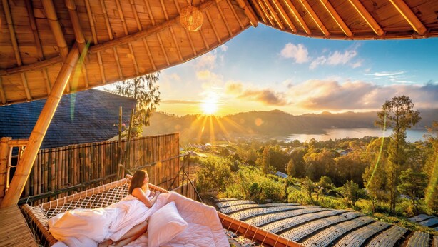 A hammock bed under a bamboo roof with a view of the sunset over a mountainous landscape. - The Dewi Eco Bamboo Villa (Kintamani)