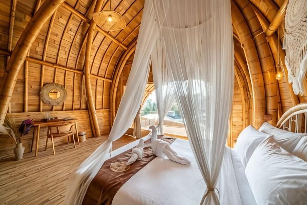 A room with a bed, a table, and a chair, all in a rustic wooden structure with a curved ceiling.