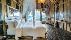 A room with a bed, a chair, a table, and a view of the mountains. - The Dewi Eco Bamboo Villa (Kintamani)