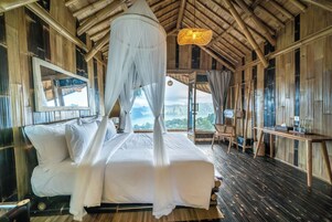 A room with a bed, a chair, a table, and a view of the mountains.