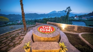 A stone bench with a circular flower arrangement and the text "THE DEWI" in the center, surrounded by a stone pathway and greenery. - The Dewi Eco Bamboo Villa (Kintamani)