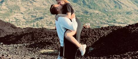 A couple embracing on a rocky terrain with a mountain in the background.