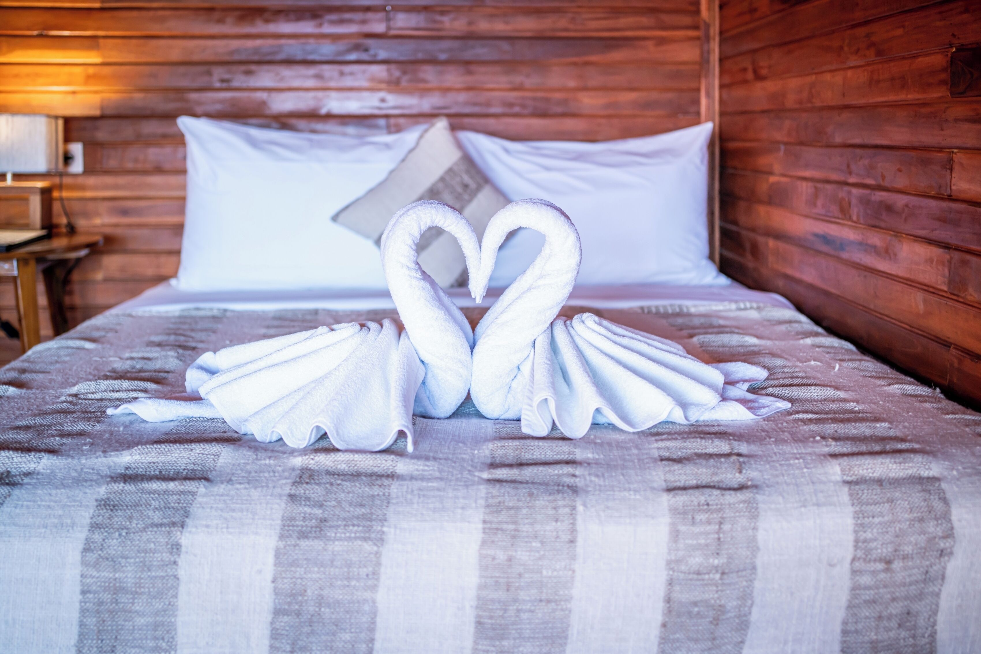 A bed with a checkered bedspread and pillows, and two towels arranged in a heart shape.