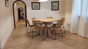 A dining area with a round table, six wicker chairs, a hanging light fixture, and two framed pictures on the wall. - Apartment 'Casa Faro' with Sea View, Wi-Fi and Air Conditioning (Puerto Pollensa)